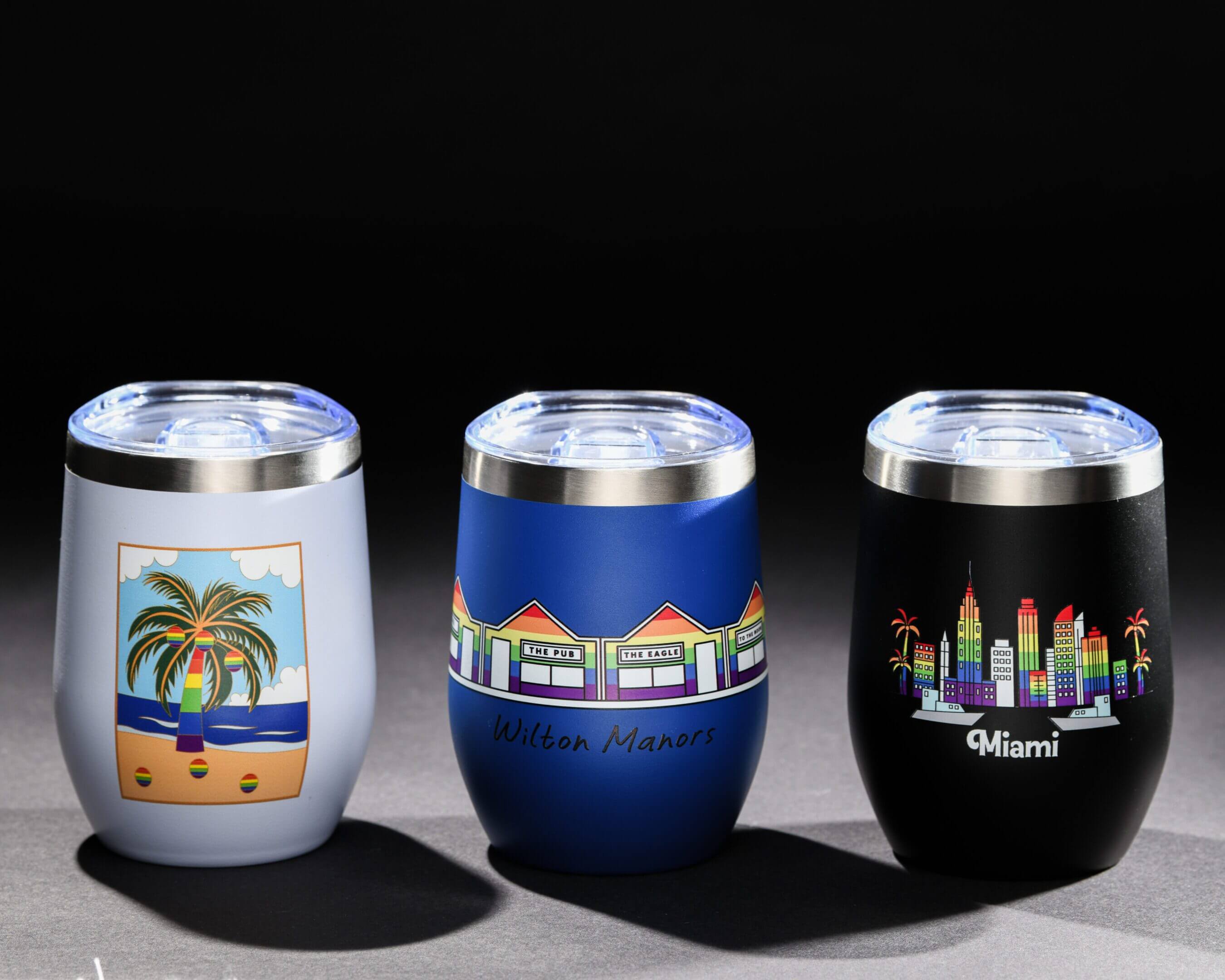 Three colorful drink tumblers with scenic designs on a black background.